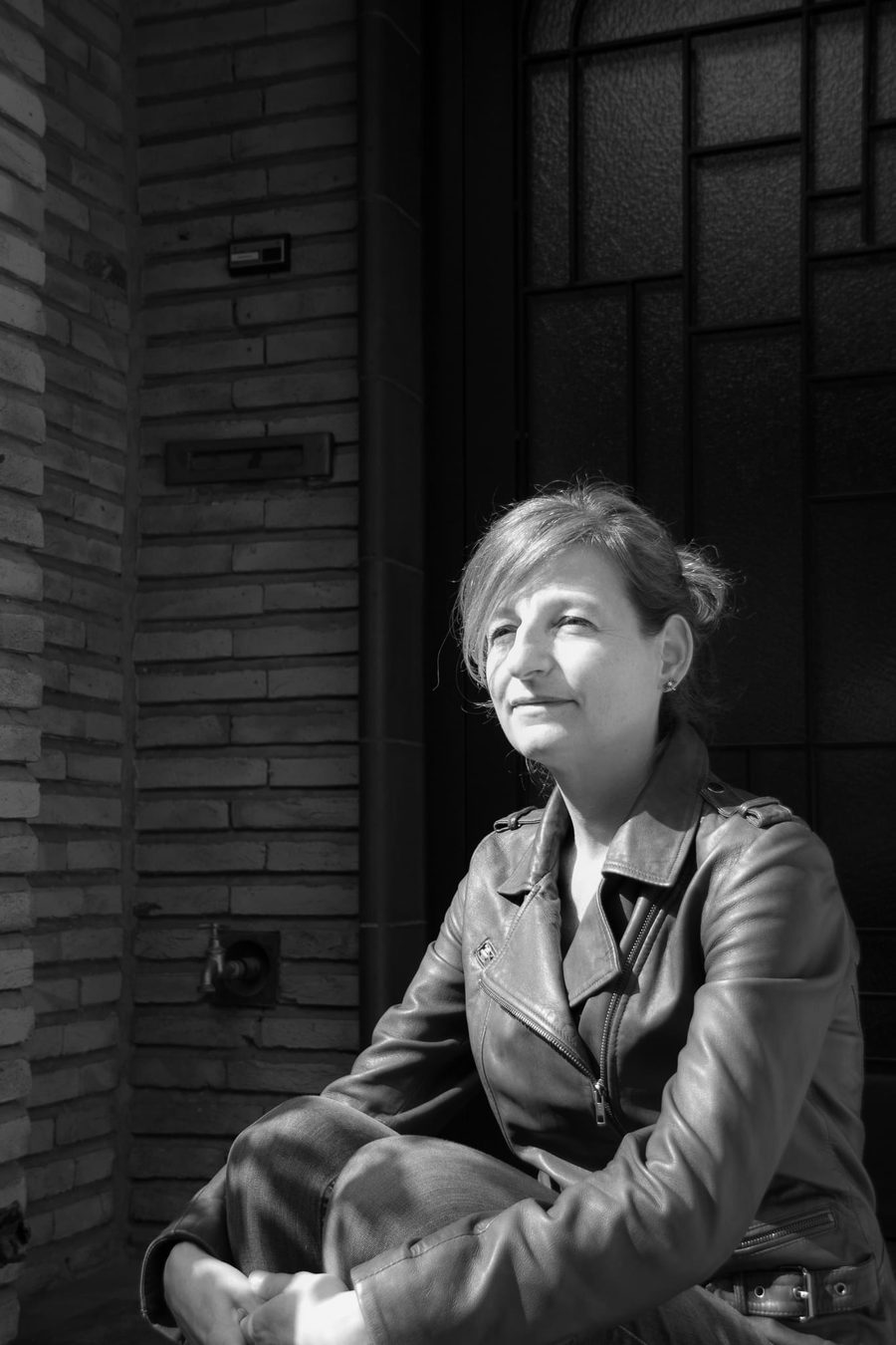 Rosy Hoppe zit in de zon op de drempel van een voordeur, met een lederen jas aan